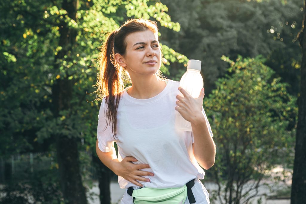 Woman walking outdoors with her hand resting on her abdomen.